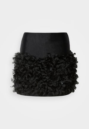 Sort nederdel med en tætsiddende top og en frynset bund lavet af lagdelt blomsterlignende stof, der skaber tekstur og volumen.