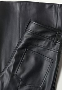 Pantalon noir en similicuir avec poche avant et passants de ceinture, plié et posé à plat sur une surface en similicuir noir assortie.