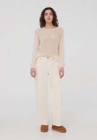 Maglione beige chiaro lavorato a maglia con vestibilità ampia e scollo rotondo, abbinato a pantaloni a gamba larga color bianco sporco e stivaletti alla caviglia in camoscio marrone.