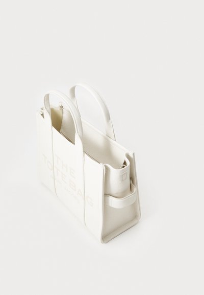 Geantă tote din piele albă cu un design structurat, având două mânere și text embosat. Textură netedă cu o estetică minimalistă.