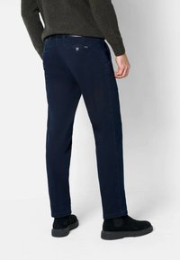 Navyblaue Chinos mit geradem Schnitt, ausgestattet mit seitlichen Taschen, einer geknöpften Gesäßtasche und einer glatten Textur. Kombiniert mit schwarzen Stiefeln.