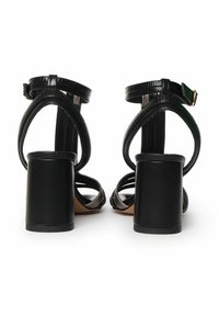 Zwarte hoge hakken sandalen met een glanzende leren afwerking, voorzien van een enkelbandje, open achterkant en een chunky vierkante hak.