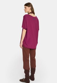 Magenta oversize t-shirt z krótkimi rękawami i okrągłym dekoltem, w połączeniu z brązowymi dopasowanymi spodniami i teksturowanymi ocieplaczami na nogi.