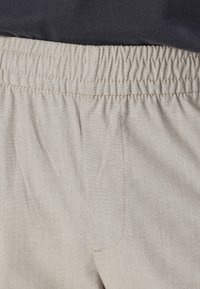 Pantalons beige à taille élastique avec une texture subtile et une poche latérale. L'élasticité permet un confort et une flexibilité dans l'ajustement.