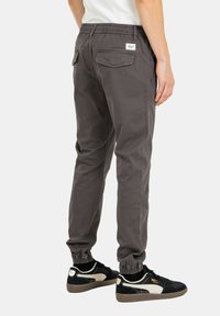 Pantalones de chándal grises con cintura y puños elásticos, que cuentan con bolsillos laterales y traseros. La modelo los combina con zapatillas negras con detalles en blanco.