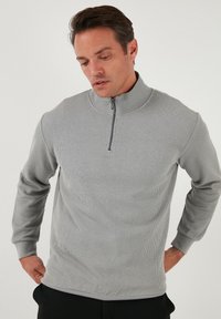 Light gray pullover with a high collar and a zip closure. Made of ribbed fabric, featuring long sleeves and a fitted silhouette.