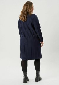 Tumesinine kootud kleit tekstuuriga kaablidisainiga, pikkade varrukatega, küljes lõhedega ja sirge lõikega, koos mustade pahkluu saapadega.