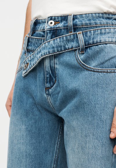 Τζιν παντελόνι ανοιχτού μπλε χρώματος με ελαφρώς ξεθωριασμένη υφή, διαθέτει κούμπωμα με κουμπί, θηλιές για ζώνη και ορατή ραφή κατά μήκος των ραφών.