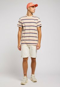 Striped beige t-shirt with navy and red lines, light shorts, and a coral cap. Casual sneakers complete the outfit. Simple design features.