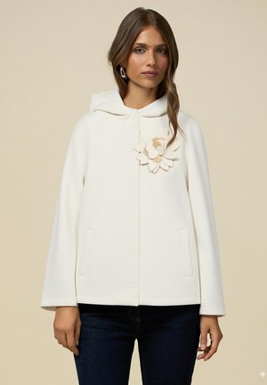 Weißer Kapuzenjacke mit einer Vorderknopfleiste, zwei seitlichen Taschen und einem dekorativen Blumenakzent auf der Brust. Weiche, glatte Textur.