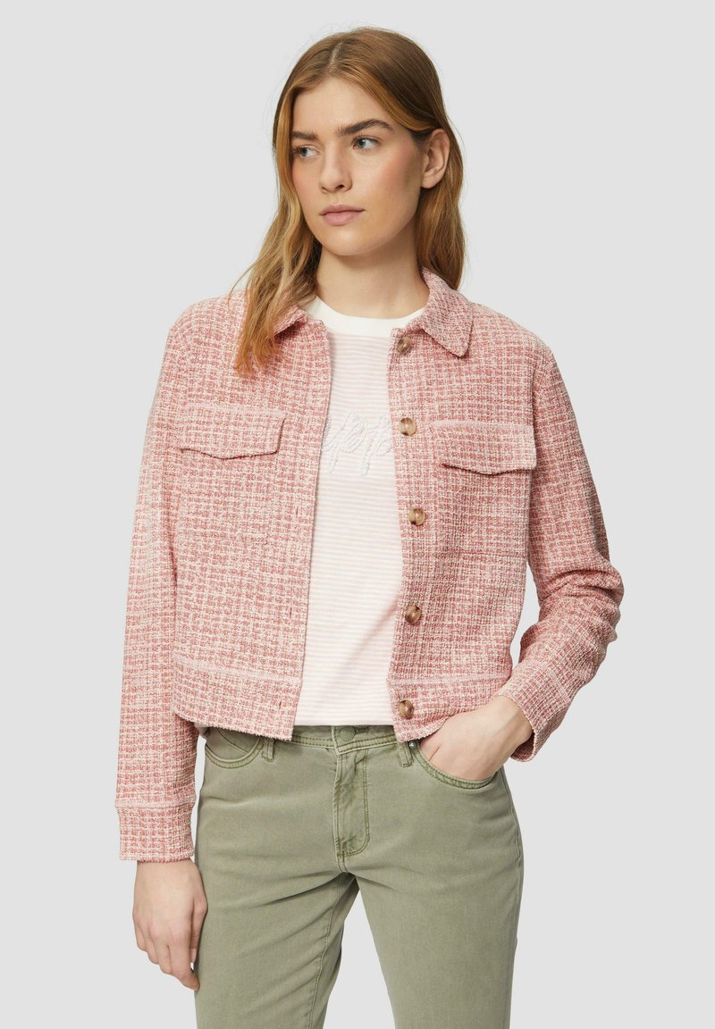 Roze geweven jasje met twee borstzakken, bruine knopen en lange mouwen. Draag het over een gestreept shirt en olijfgroene broek.