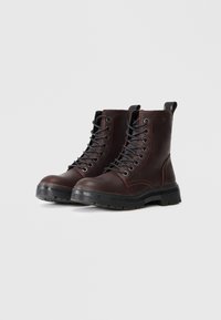 Brune lær ankle boots med sorte snørebånd, en teksturert overflate, polstret krage og robust svart gummisåle.
