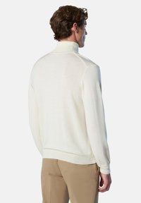 Suéter de color crema con cuello alto, mangas largas y una textura suave. Presenta un diseño ajustado y un dobladillo y puños acanalados.