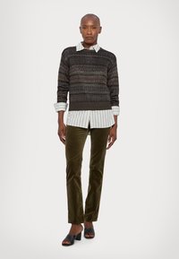 Knit sweater in dark tones with a geometric pattern, layered over a white striped shirt; paired with dark green corduroy pants and black sandals.