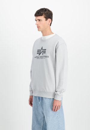 Sweatshirt gris clair avec des poignets et un ourlet côtelés. Présente un logo noir "ALPHA INDUSTRIES" et un graphique sur le devant, coupe décontractée, en mélange de coton.