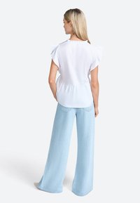 White blouse with ruffle sleeves, cinched waist, paired with light blue wide-leg jeans. Smooth texture, casual design.