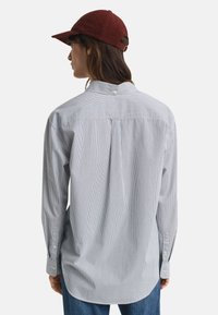 Persona che indossa un berretto di corduroy rosso e una camicia a maniche lunghe a righe sottili blu chiaro e bianca vista da dietro.