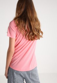 Kortärmad t-shirt i mjuk rosa bomull, med rund halsringning och en avslappnad passform. Bakvy med synligt vågigt hår och textilstruktur.