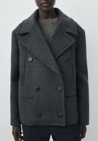 Cappotto grigio in misto lana doppiopetto con ampi revers, due tasche e bottoni neri. La consistenza appare morbida e calda.