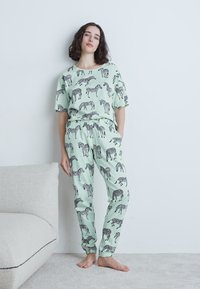 Hellgrünes Schlafanzugset mit einem lässigen Kurzarmoberteil und passenden Hosen, beide mit schwarzen Zebramustern verziert.