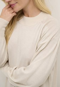 Helle beige, gestrickte Pullover mit rundem Ausschnitt und langen, leicht gepufften Ärmeln. Besitzt einen dezenten Schimmer in der Stoffstruktur.