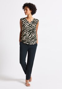 Top senza maniche in un motivo zebra nero e beige, design a scollo a V; abbinato a pantaloni blu navy e sandali beige, tessuto liscio con caduta.