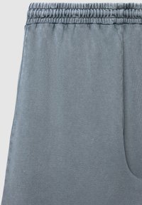 Pantalons de survêtement gris avec une taille élastique et une poche latérale, fabriqués en tissu doux et texturé, avec une finition lisse.