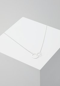 Collar de plata con una cadena delicada, que presenta dos anillos redondos superpuestos de diferentes tamaños, textura suave y un diseño minimalista.