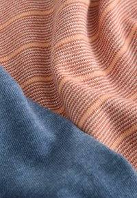 Nærbillede af blødt strikket stof med fersken- og hvide striber ved siden af ensfarvet lyseblåt strikket stof, der viser tekstur og folder.