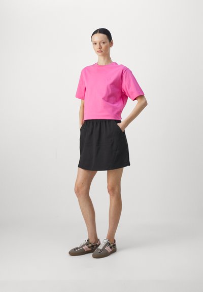 Lys rosa bomull t-skjorte med korte ermer, sammen med et svart skjørt med elastisk midje som har sidelommer. Brune og rutete sneakers.