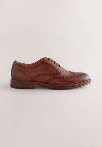 Chaussure Oxford en cuir marron avec détails brogués, bout rond et petit talon empilé. Présente des variations de surface lisses et texturées.