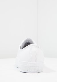 Fehér bőr sportcipő sima textúrával és diszkrét varrással. Alacsony profilú, a saroknál dombornyomott "Converse All Star" logóval rendelkezik.