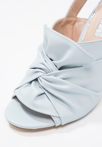 Chaussure slingback en cuir bleu clair avec un design noué à l'avant et un bout ouvert. Texture lisse et style minimaliste.