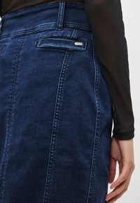 Tamsaus džinso sijonas su apta alkoholiu siluetu, turintis galines kišenes ir subtilias siuvimo detales. Lygios tekstūros, vidutinio aukščio liemuo.