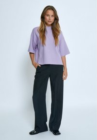 Top in maglia viola con maniche larghe, abbinato a pantaloni neri a gamba dritta. Il top ha un collo alto ed è indossato in modo rilassato.