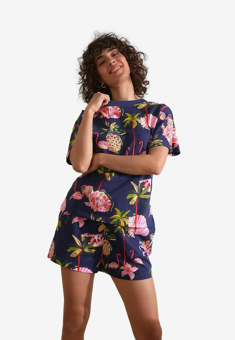 Ensemble coordonné en marine à motifs floraux comprenant des manches courtes et un short, orné de fleurs roses, de feuilles tropicales et d'ananas. Matière en mélange de coton.