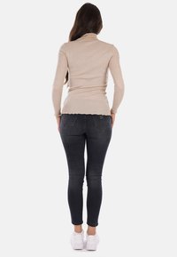 Top a maniche lunghe a dolcevita beige, aderente, realizzato in materiale a coste, abbinato a jeans skinny scuri e sneakers bianche, visto da dietro.
