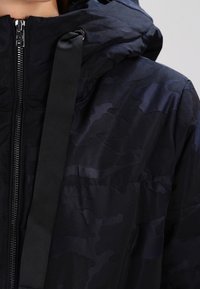 Chaqueta de camuflaje de la marina con un cuello alto, cierre de cremallera y un acento de correa negra contrastante en el hombro.