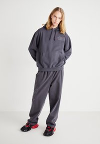 Grå hettegenser med lomme foran og "STAR WARS"-logo. Kombinert med matchende grå joggebukser. Svarte og røde joggesko.