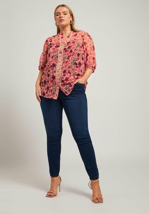 Blumenbluse in rosa und lila Tönen, aus leichtem Stoff, mit Knopfverschluss und kurzen Ärmeln. Kombiniert mit dunkelblauen Skinny Jeans.