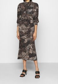 Långärmad skjortklänning i svart, brunt och cremefärgat djurmönster, med krage, rynkad midja och fladdrig kjol. Tillsammans med svarta klacksandaler.