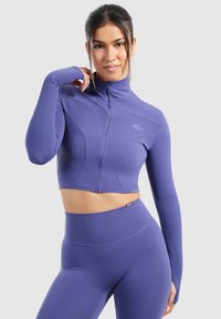 Lilla crop jakke med lange ærmer, høj krave og lynlås foran. Har et tætsiddende design og glat tekstur, parret med matchende højtaljede leggings.