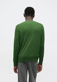 Zielony prążkowany sweter z okrągłym dekoltem i długimi rękawami, wykonany z miękkiego materiału o fakturowanym wykończeniu. Widok od tyłu.