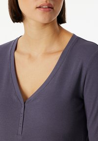 Purple ribbed long-sleeve top with a deep V-neckline and three buttons on the placket; smooth texture with subtle stretch.