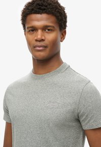 Grijze crewneck t-shirt met korte mouwen. Zachte stofstructuur. Klein geborduurd logo op de linker borst. Eenvoudig, klassiek ontwerp.