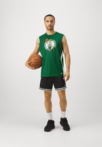 Πράσινη αμάνικη μπλούζα μπάσκετ με γραφικό των Boston Celtics, συνδυασμένη με μαύρα σορτς με λευκή περιφέρεια και μαύρα αθλητικά παπούτσια.