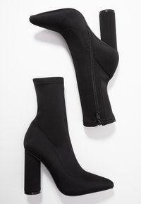 Bottines noires à bout pointu, talon bloc haut et fermeture éclair, confectionnées en tissu lisse et extensible.