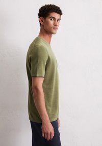 Oliwkowa koszulka z krótkim rękawem, okrągłym dekoltem, dopasowany krój, fakturowany materiał oraz kontrastowe przeszycia na krawędziach rękawów.