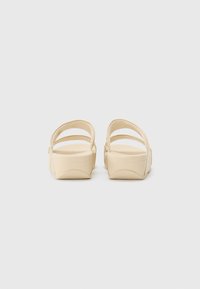 Beige plattform sandaler med to tynne stropper over toppen, glatt materiale, og en kraftig såle med en lett buet form.