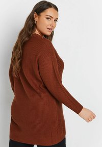 Brun stickad tröja med avslappnad passform, långa ärmar och en strukturerad mönstring. Har sidslitsar och rund halsringning.